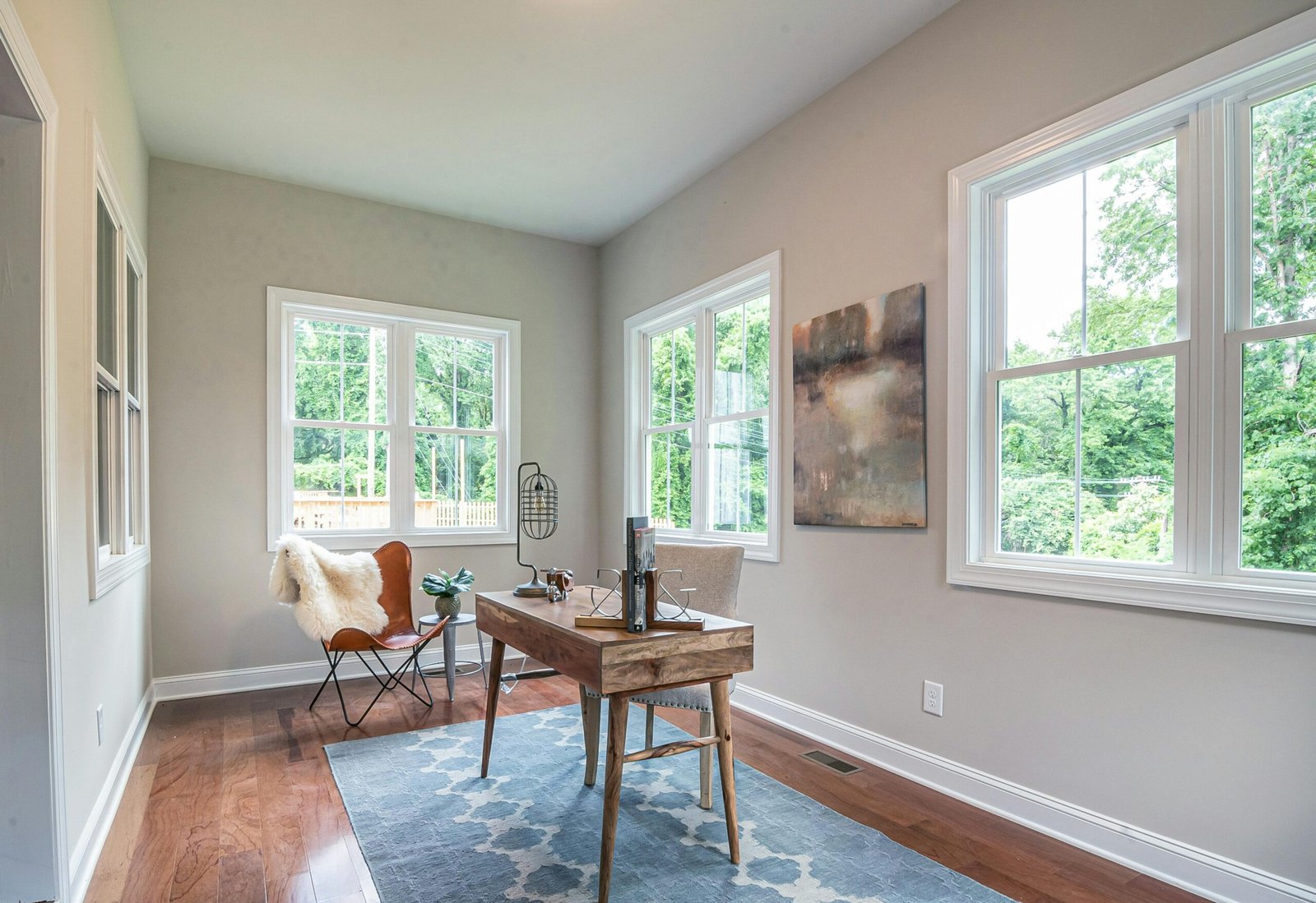 How to Stage Like a Pro Using Neutral, Updated Rugs A sunny home office featuring modern furniture, decor, and abundant natural light from large windows.
