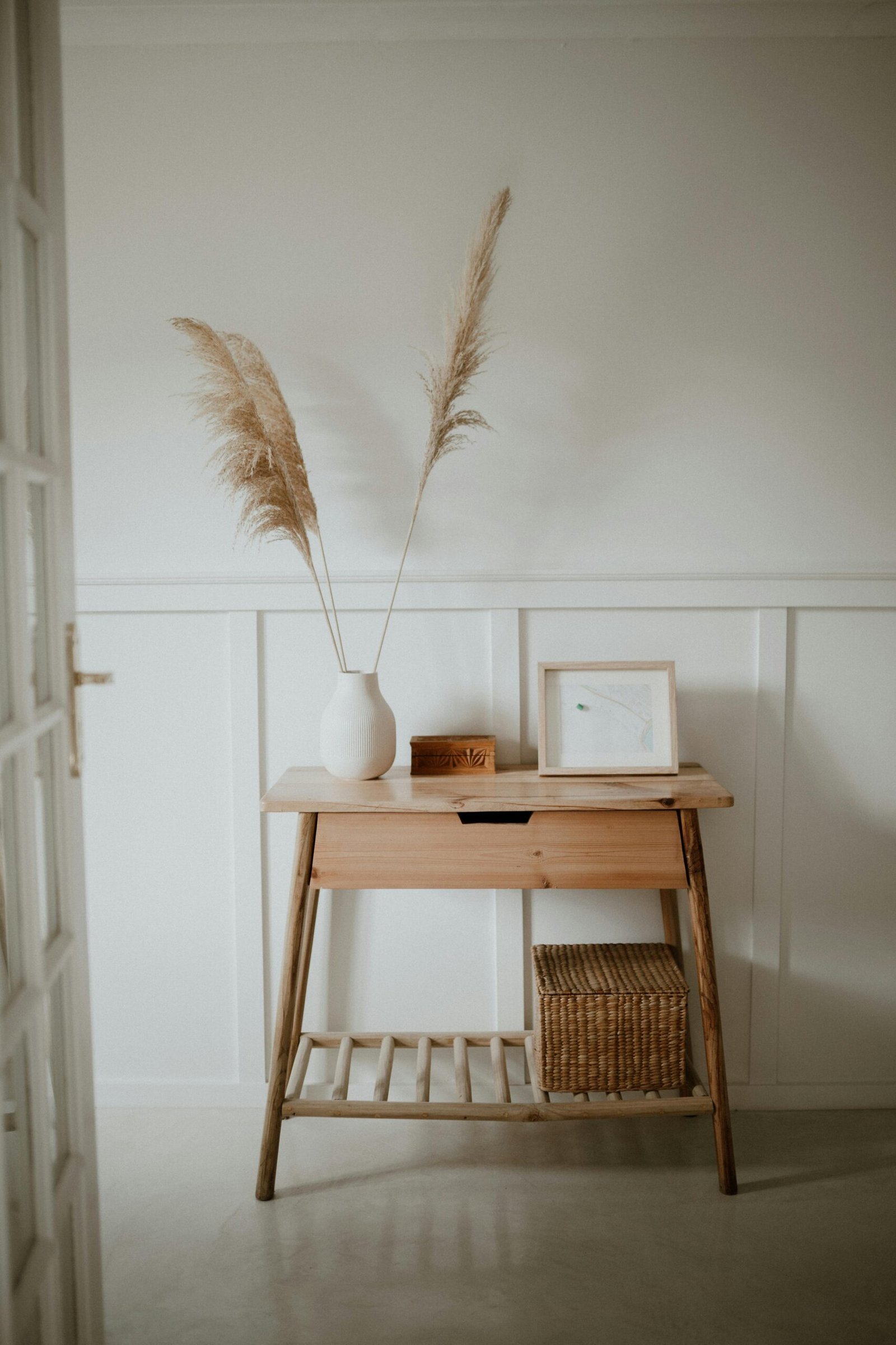A serene minimalist interior features a wooden console table with pampas grass in a vase.